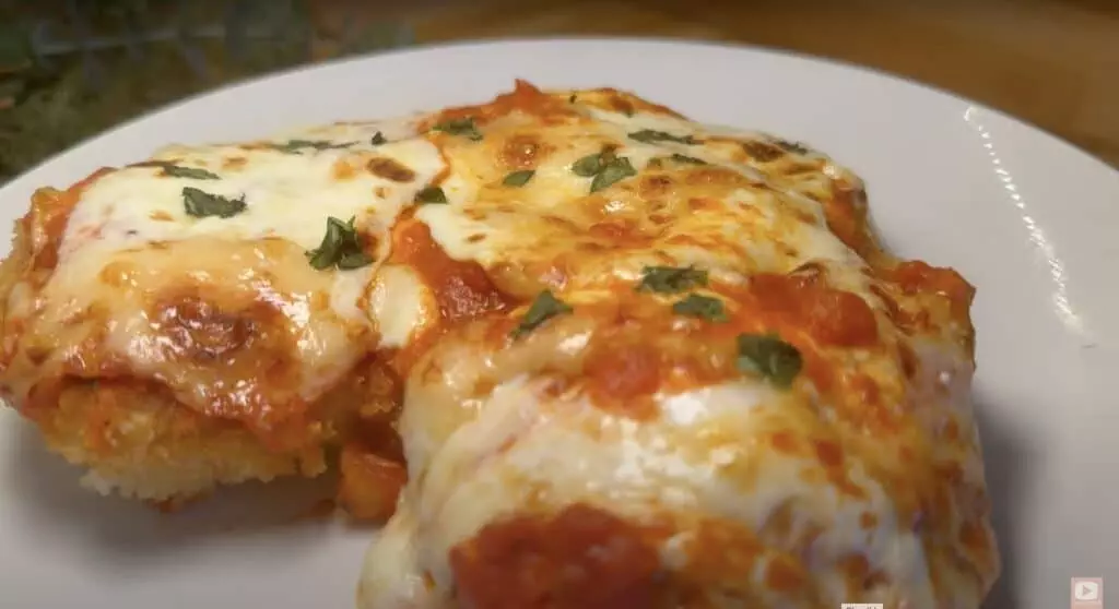 Delicious chicken parmesan topped with melted cheese and herbs on a white plate.